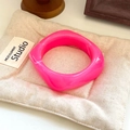 Close-up of a glossy pink resin square bangle resting on a soft quilted cushion - Geometric Rhombus / Inner Diameter 65mm / Rose Red