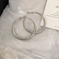 Close-up of minimalist silver circular hoop earrings on a decorative white paper backdrop - Silver Needle Silver Large