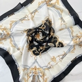 Dettaglio di un foulard quadrato setoso con motivi barocchi dorati e pieghe eleganti - Nero Bianco e Oro