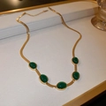 Detailed view of golden snake chain necklace with five oval green emerald stones on white leather - Emerald Necklace