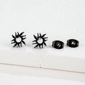 Detail of matte black stainless steel sun earrings on a textured stone display pedestal - Flame Sun / Black