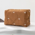 Detail showing brown quilted makeup bag with white bow embroidery and metallic zipper - Caramel color