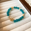 Detailed view of teal beaded bracelet with gold accents and dual ring clasp on velvet - Teal Round Beads With Gold Buckle