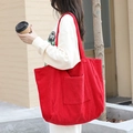 Large red corduroy tote bag with front pocket shown in an outdoor casual setting - Red