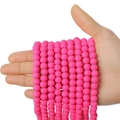 Rosafarbene runde Perlen aus Fimo für DIY-Schmuck in einer Hand auf weißem Hintergrund - Dunkelrosa