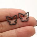Close-up of minimalist black hollow butterfly stud earrings displayed on a finger - 670 Hollow Winged Butterfly / Black