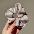 Detail of silver silk satin scrunchie showing glossy pleated texture and elegant drape - Space Gray