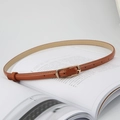 Detailansicht eines schmalen braunen Ledergürtels mit goldener Schnalle auf einem Buch - Khaki