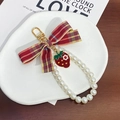 Detalle de llavero con lazo rojo, colgante de fresa y perlas sobre un plato de cerámica - Lazo de Cuadros