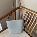 Silver-gray woven straw bucket bag with brown leather shoulder strap on a wooden chair - Gray
