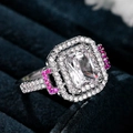 Macro view of princess cut clear gemstone ring with pink side stones on blue velvet - US 6 / White Gold