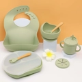 Green silicone baby feeding set with suction plate, bowl, bib, and cups on white display stand - Olive Green