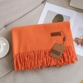 Solid orange cashmere-feel scarf with tassels and leather tag on a soft sofa - Orange