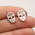 Close-up of gothic skull stud earrings in silver finish held between fingers for size - Steel