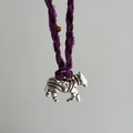 Macro shot of a zebra-shaped metal pendant with purple and brown braided cord - Silver Zebra Pendant / Purple Rope