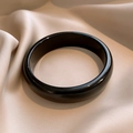 Polished black resin round bangle displayed on elegant champagne silk fabric - Black