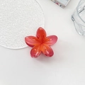 Detail view of a vibrant red and orange gradient flower hair claw on a white desk - Watermelon Red Plumeria