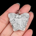Handheld view of a carved butterfly pendant in white turquoise with marble texture - Howlite