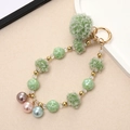 Detail showing plush green pompom and colorful faux pearl beads on a gold keychain - Green