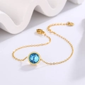 Macro shot of a minimalist 18k gold-plated bracelet with a round blue crystal centerpiece - Gold + Lake Blue Zirconia