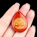 Red jasper teardrop pendant with golden Tree of Life carving held by hand - Red Jasper