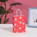 Detail of red paper gift bag with white paw print and soft rope handles in warm setting - H21*L15*W8 / Red