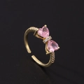Vue macro des pierres roses en cœur et du détail en nœud sur une bague dorée réglable - Style Doux Double Coeur