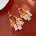 Macro shot of bohemian gold leaf earrings with cream tassels on red satin background - Hook Style / Gold/Off-white