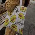 Detail van een witte canvas draagtas met avocado-opdruk vastgehouden door een persoon - Avocado