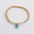 Close-up of golden beaded bracelet with white pearls and a sky blue heart pendant - Blue
