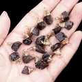 Garnet red raw stone pendants with gold plated caps held in hand on black background - Garnet