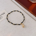 Detail of bohemian black and gold beaded bracelet with shell pendant on linen background - Bracelet-Black-Conch