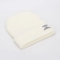 Detalle del tejido de un gorro crema con textura de canalé y etiqueta de parche de moda - Blanco