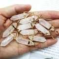 Macro-opname van witte kristallen zeshoekige hangers met gouden metalen sluitingen in de hand - Bergkristal