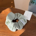 Detail of light green puff fabric scrunchie with button and woven label on wood table - Grey Green Button Scrunchie