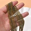 Close-up of sparkling 2mm gold faceted crystal glass spacer beads held by hand for DIY jewelry - Gold Champagne