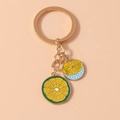 Detail of two colorful enamel lemon slice pendants on a gold-toned metal keychain - Green