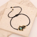 Makro-Detail eines handgewebten Hamsa-Hand-Armbands mit Evil Eye-Perlen auf Steinbelag - Schwarz