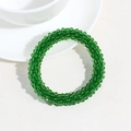 Detail eines grünen Perlenarmbands mit facettierten Kristallen neben einer Tasse - Grün
