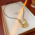 Détail d'un pendentif en métal doré en U avec cordon en cuir noir sur un plateau en lin - Corde Noire-Pendentif Doré