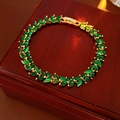 Detailed macro view of green marquise gems in a gold leaf setting on a luxury wooden box - Green