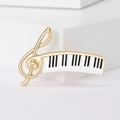 Dettaglio ravvicinato della spilla dorata con chiave di violino e tasti di pianoforte - Oro