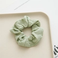 Close-up of light green pleated polyester fabric scrunchie on a beige tray - Bean Green