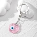 Close-up of pink resin Evil Eye pendant keychain on a minimalist white texture base - Transparent Pink Glass Eye