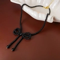 Detalle del collar de cuentas negras con lazo y flecos sobre bandeja de concha blanca - Negro