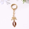 Golden keychain with brown rugby football pendant and bow charm on white background - Gold Bow American Football Style