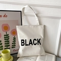 Minimalist white oxford tote bag with black print shown in a stylish room setting - White with BLACK Text