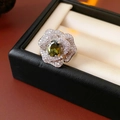 Macro-opname van zilveren bloemenring met groene ovale edelsteen en micro-pave zirkonia - Olijfgroene Ovale Zirkonia Camellia Stijl / Zilver (Groene Hoofdsteen)