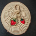 Detail view of golden strawberry keychain with enamel charm on round wooden base - Strawberry (Wood Background)