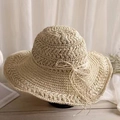 Elegant wide-brimmed beige crochet straw hat with bow detail on a light wood background - Beige